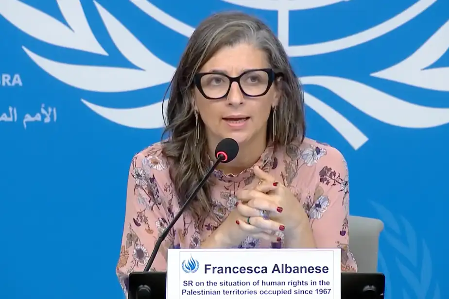Francesca assise devant un micro; derrière elle le symbole de l'ONU; elle porte une robe rosée; cheveux longs bruns; lunettes à bordures noires larges; écriteau se lit: SR on the situation of human rights in the Palestinian territories occupied since 1967.